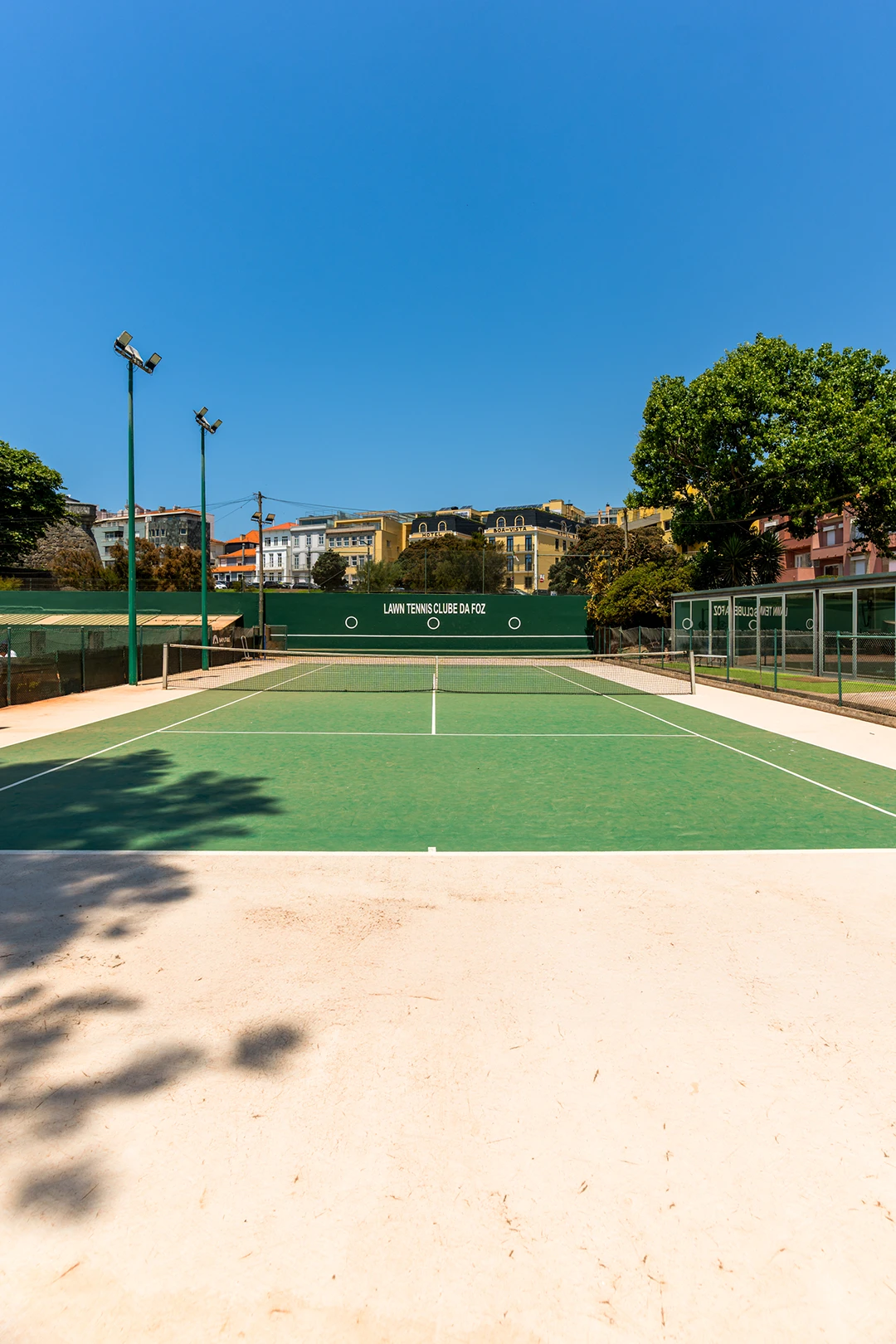 Empty outdoor tennis court with green surface under clear blue sky in an urban area.