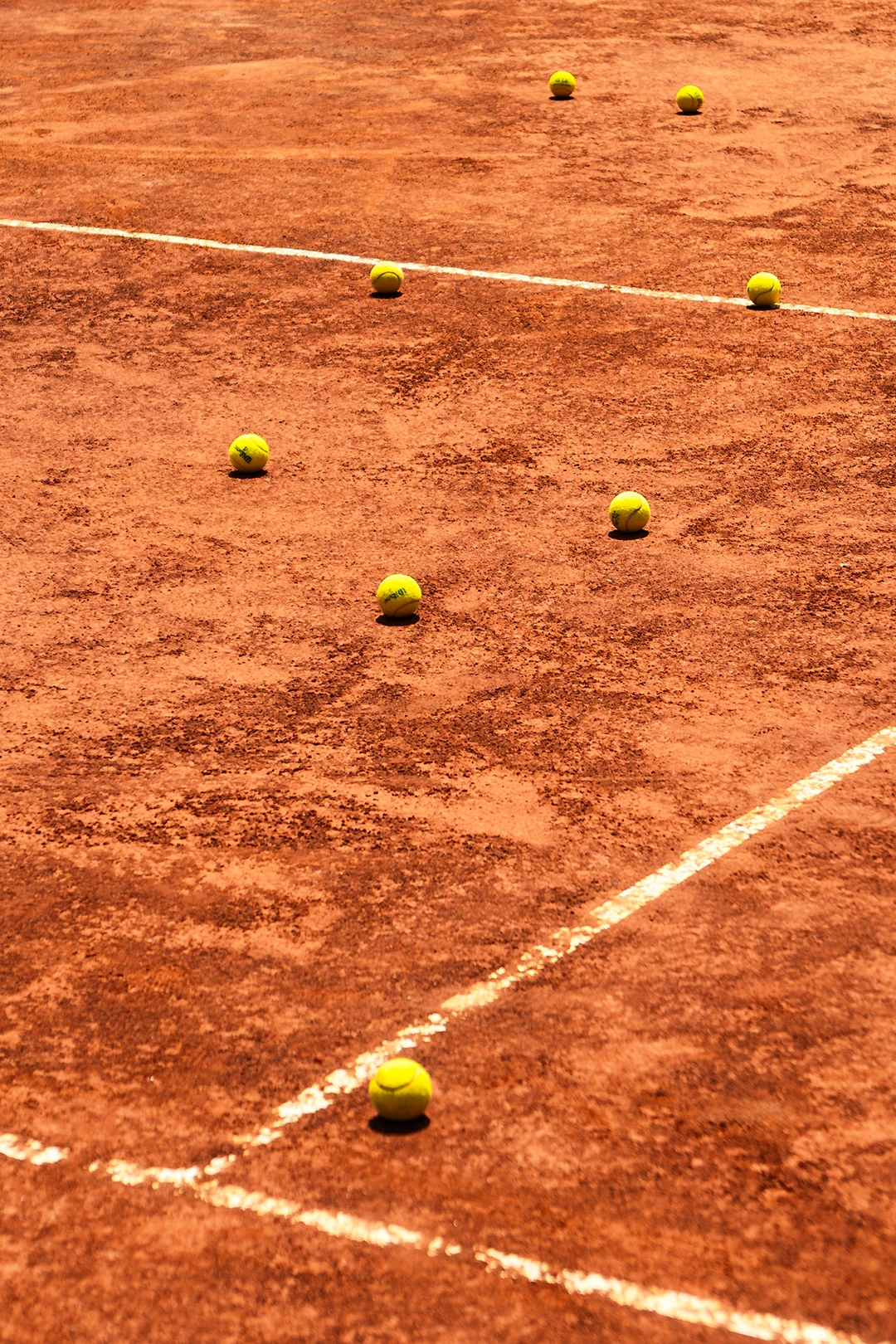 Yellow tennis balls scattered on a clay tennis court with white boundary lines.