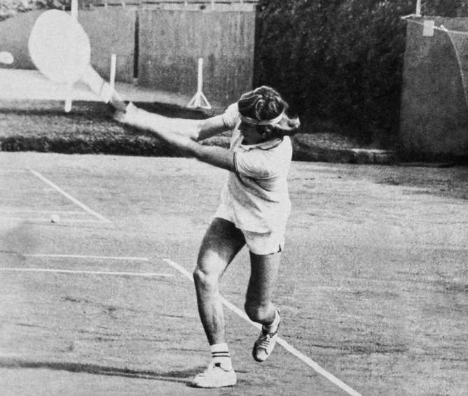 Black and white photo of a male tennis player hitting a backhand shot on a tennis court.