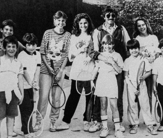 Group of children and one adult holding tennis rackets posing for a black-and-white photo.