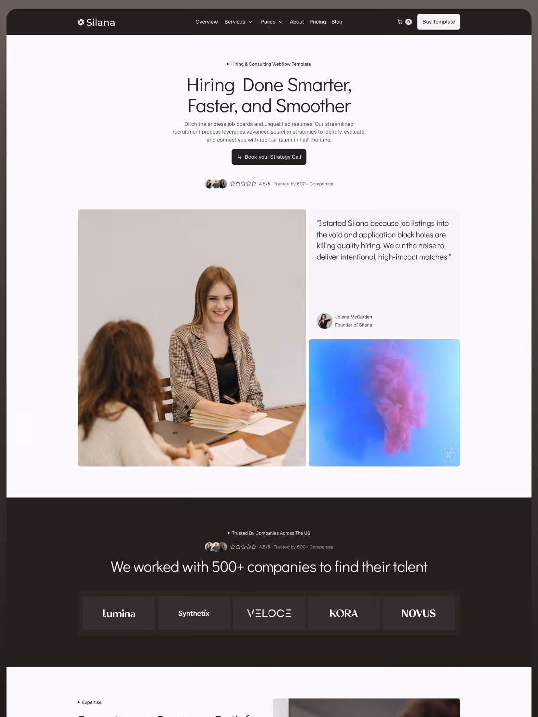 Two women at a table with notebooks and laptop, one smiling, discussing work or hiring strategy.
