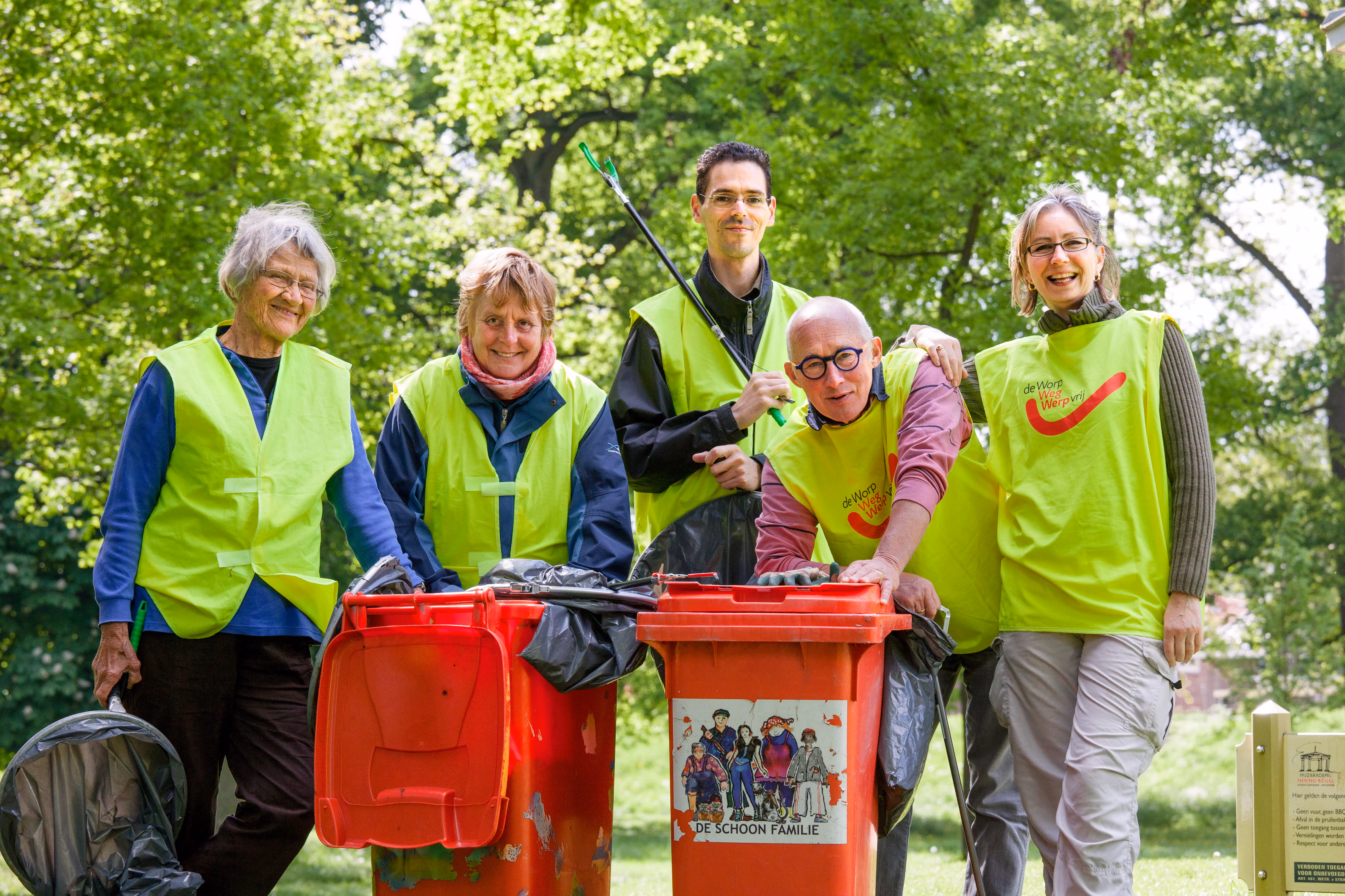 Een groep van vijf mensen poseert terwijl zij bezig zijn met een opruimactie op straat.