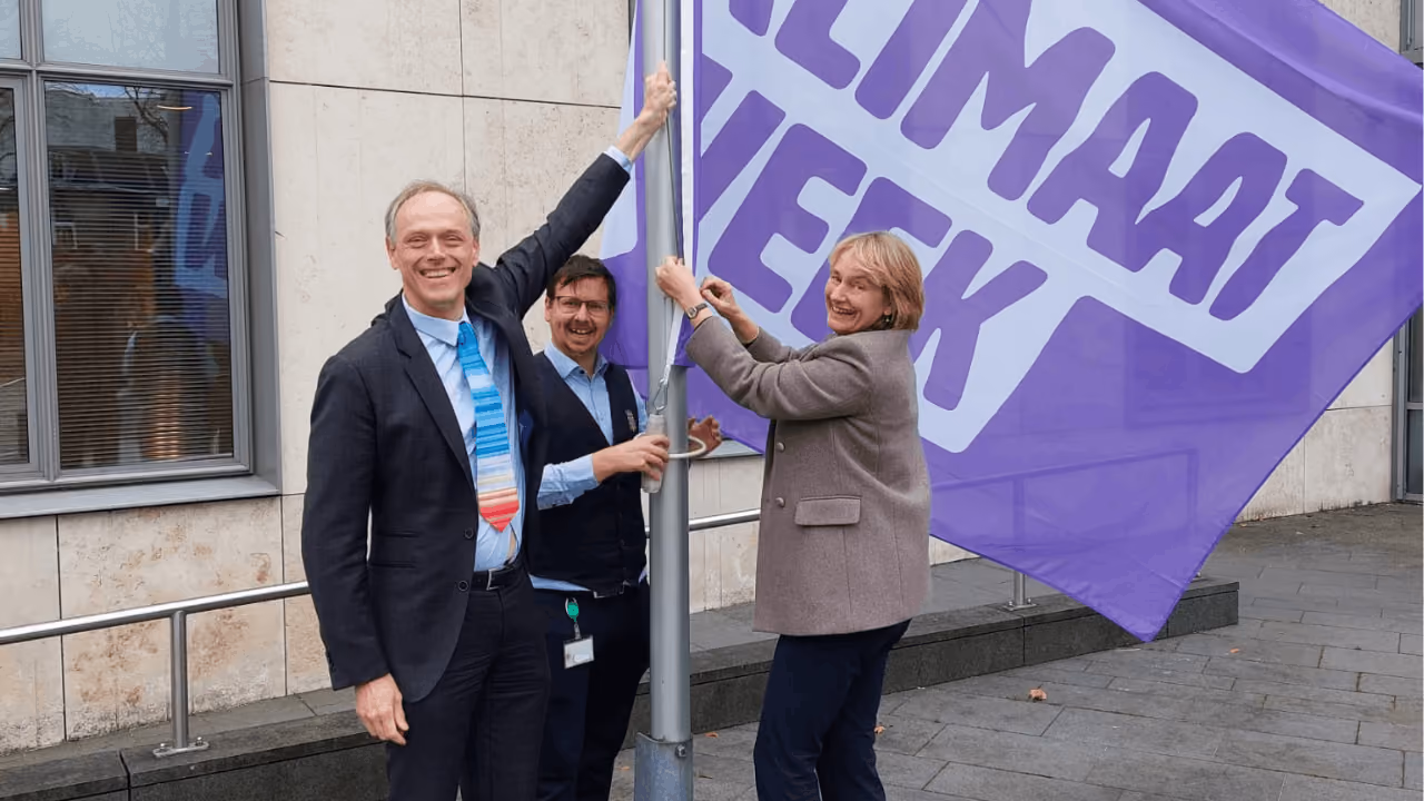 Twee ambtenaren hijsen de Klimaatweek vlag.