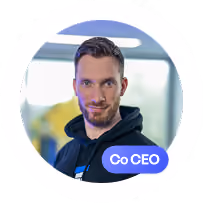 Portrait d'un homme aux cheveux courts bruns et barbe fine, portant une veste noire dans un bureau.