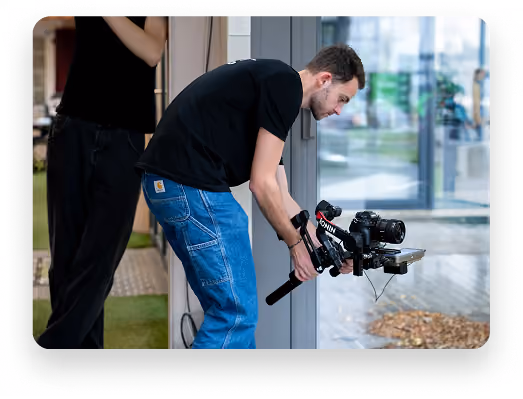 Un homme penché filme à l’aide d’une caméra professionnelle montée sur un stabilisateur.