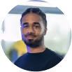 Portrait d'un homme souriant avec une barbe et des cheveux en nattes, fond flou lumineux.