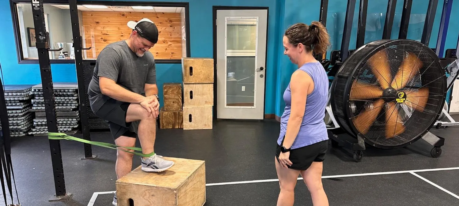Physical therapist coaching a client through a banded step-up onto a plyo box.