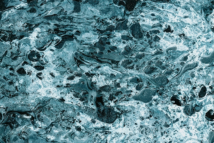 Close-up of water surface with swirling patterns and bubbles in shades of blue and white.
