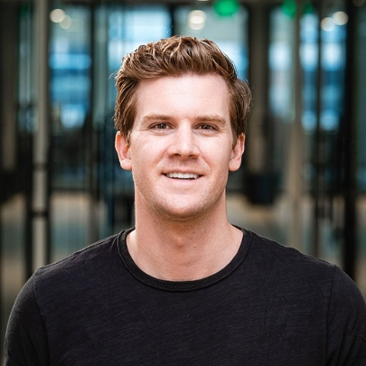 Smiling young man with short brown hair wearing a black shirt in an indoor setting.