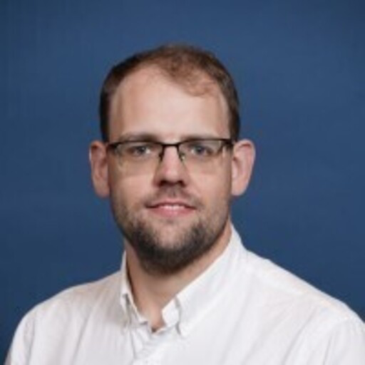 Man with glasses and short hair in a white shirt against a blue background.