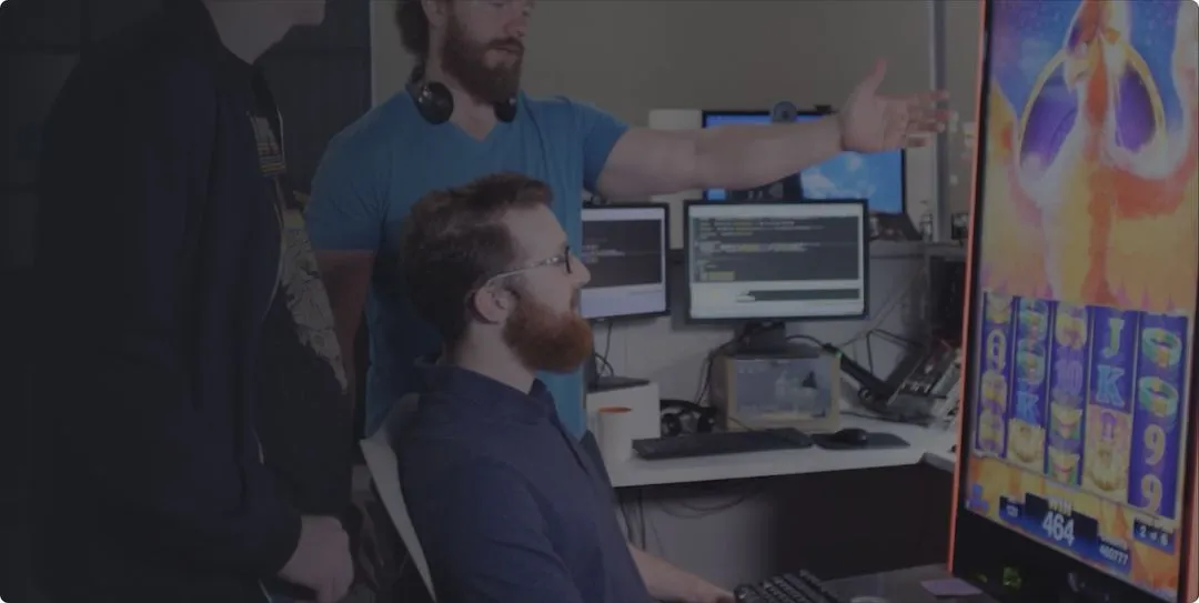 AGS developers discussing code with game screen and multiple monitors