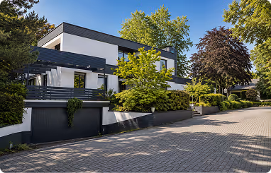 Modern white house with black accents surrounded by green trees and shrubs on a sunny day.