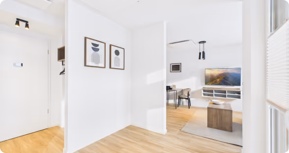 Helle Wohnung mit Holzboden, weißen Wänden, moderner Kunst und einem Wohnzimmer mit TV und Tisch.