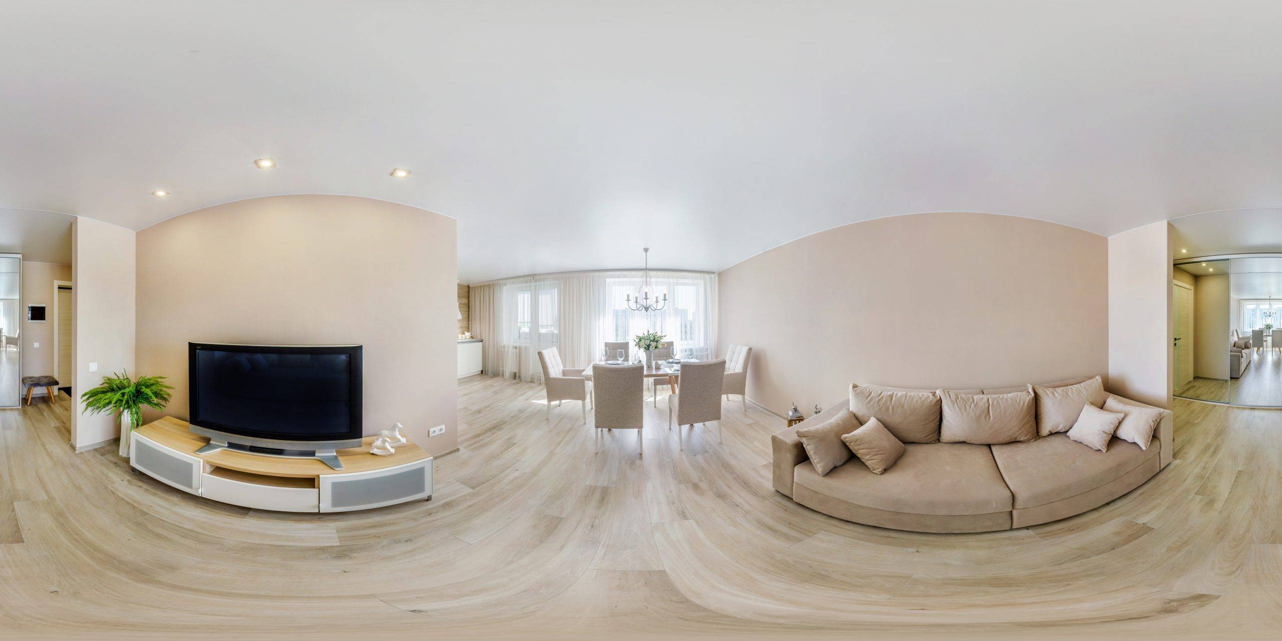 Heller moderner Wohnraum mit beiger Couch, Esstisch mit Stühlen und Flachbildfernseher.