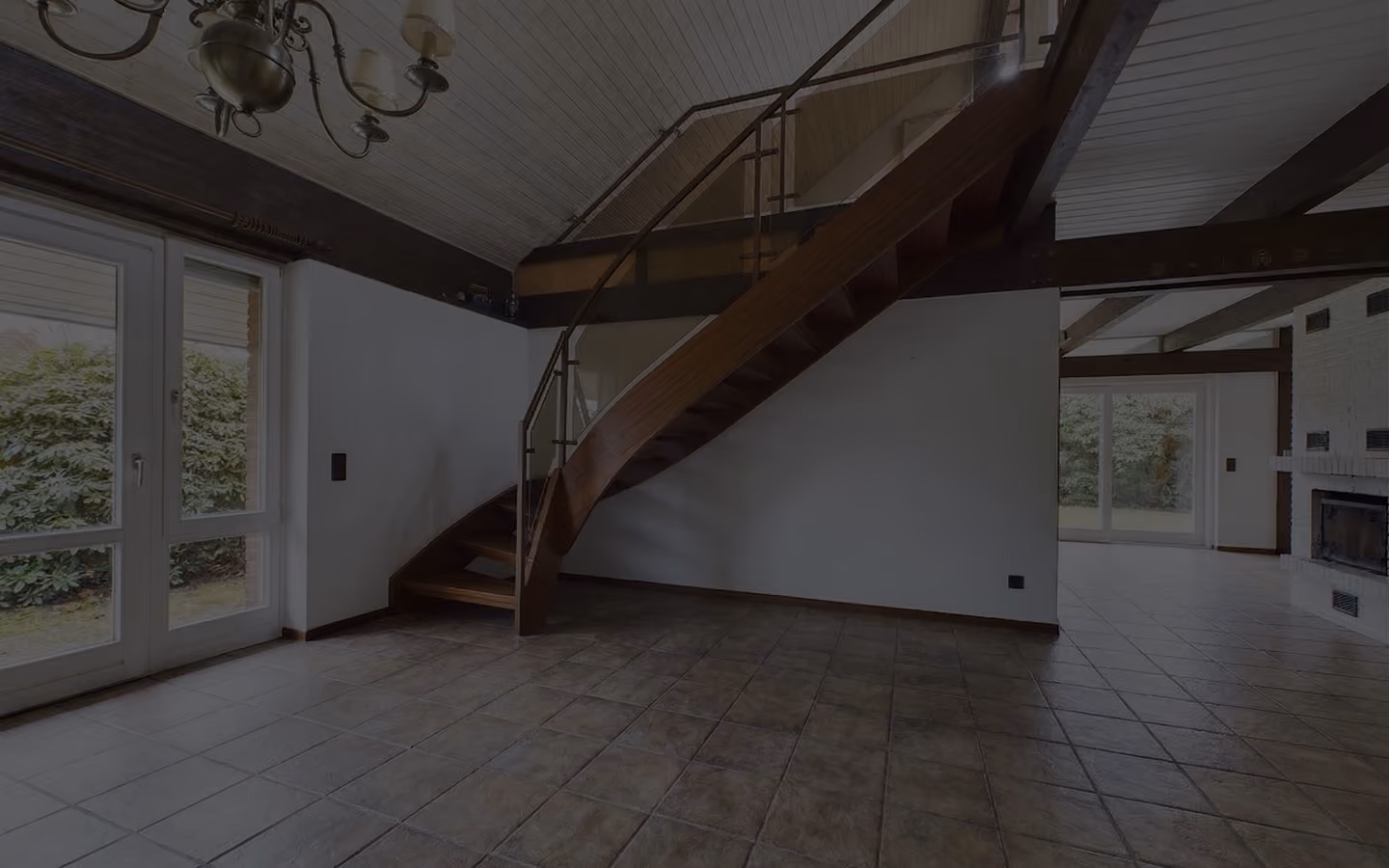 Leeres Wohnzimmer mit brauner Holztreppe, Kachelfußboden, weißen Wänden und großen Fenstern.