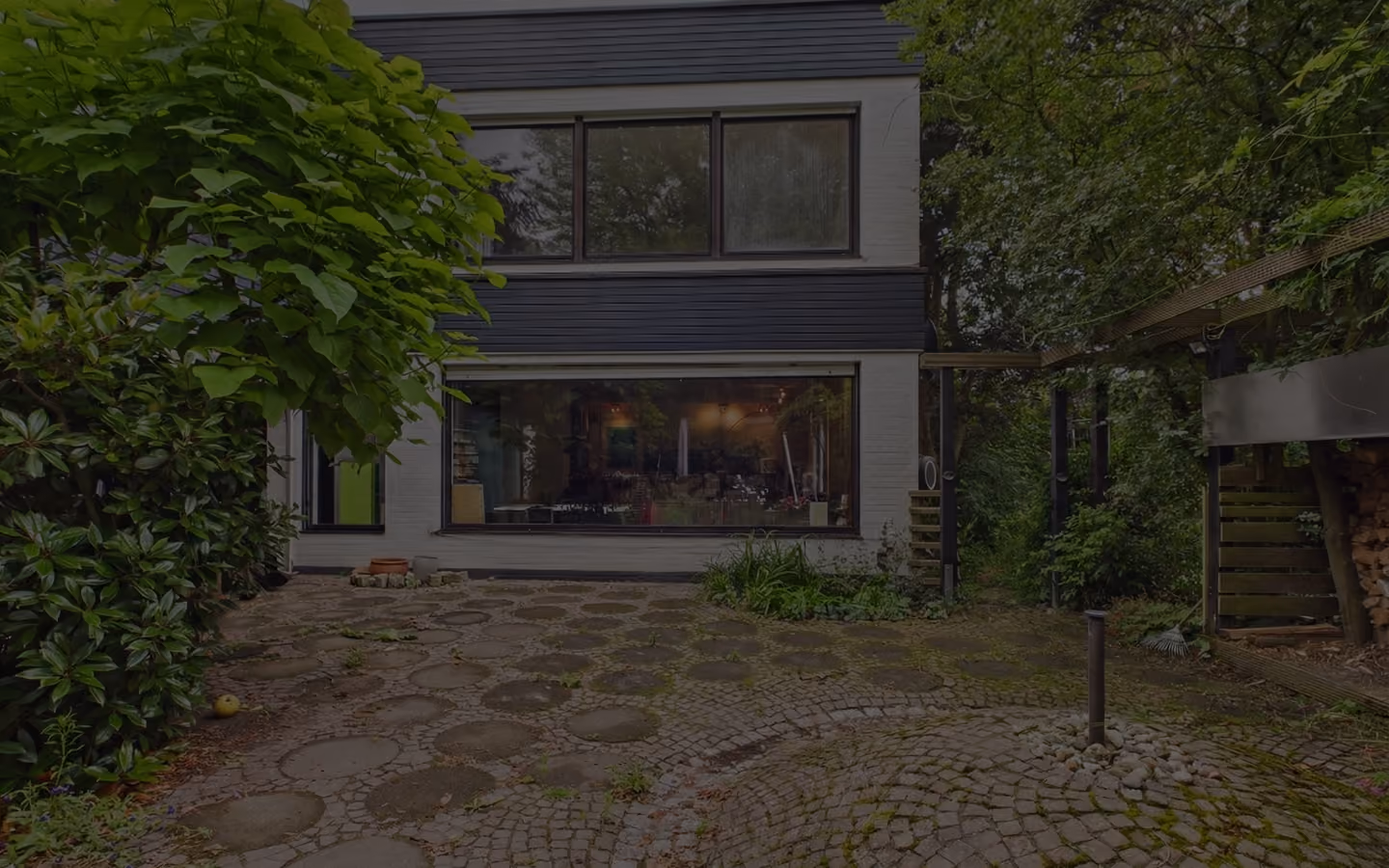 Moderner weißer Hausaußenbereich mit großen Fenstern und gepflastertem Gartenweg mit Bäumen.