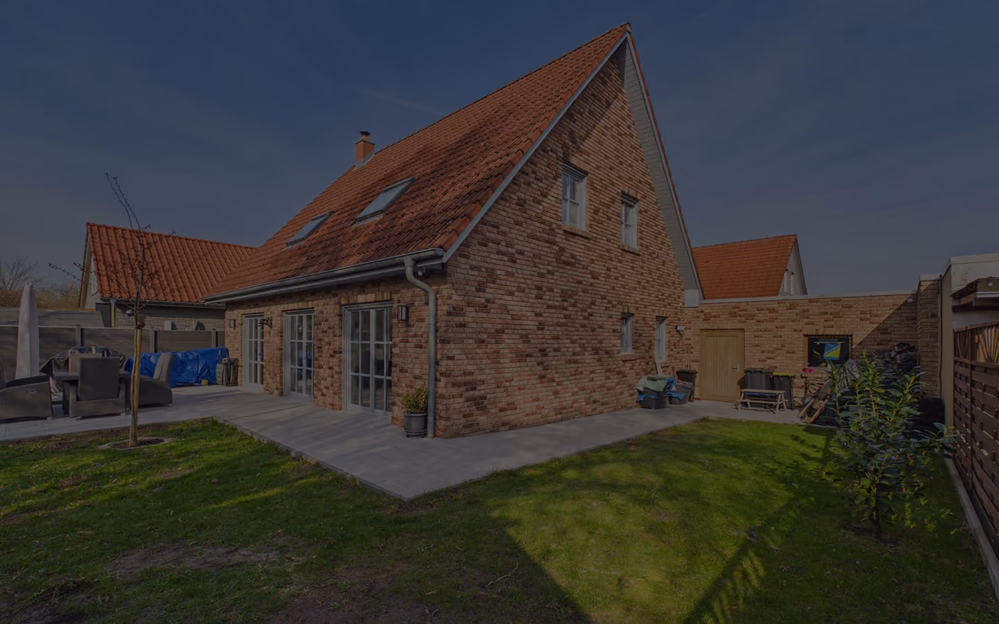 Backstein-Einfamilienhaus mit roten Ziegeldächern und Garten mit Rasen und Terrasse.