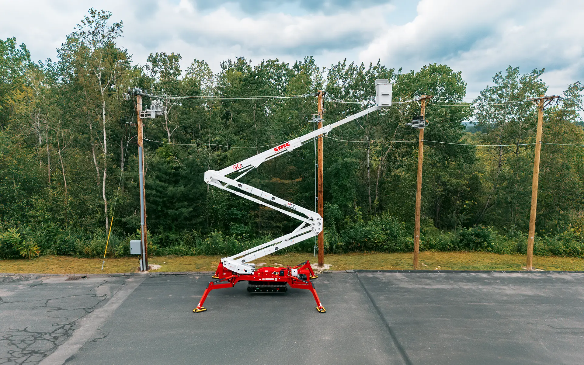 Red and white bucket truck with extended boom working on wooden power poles near trees on asphalt.