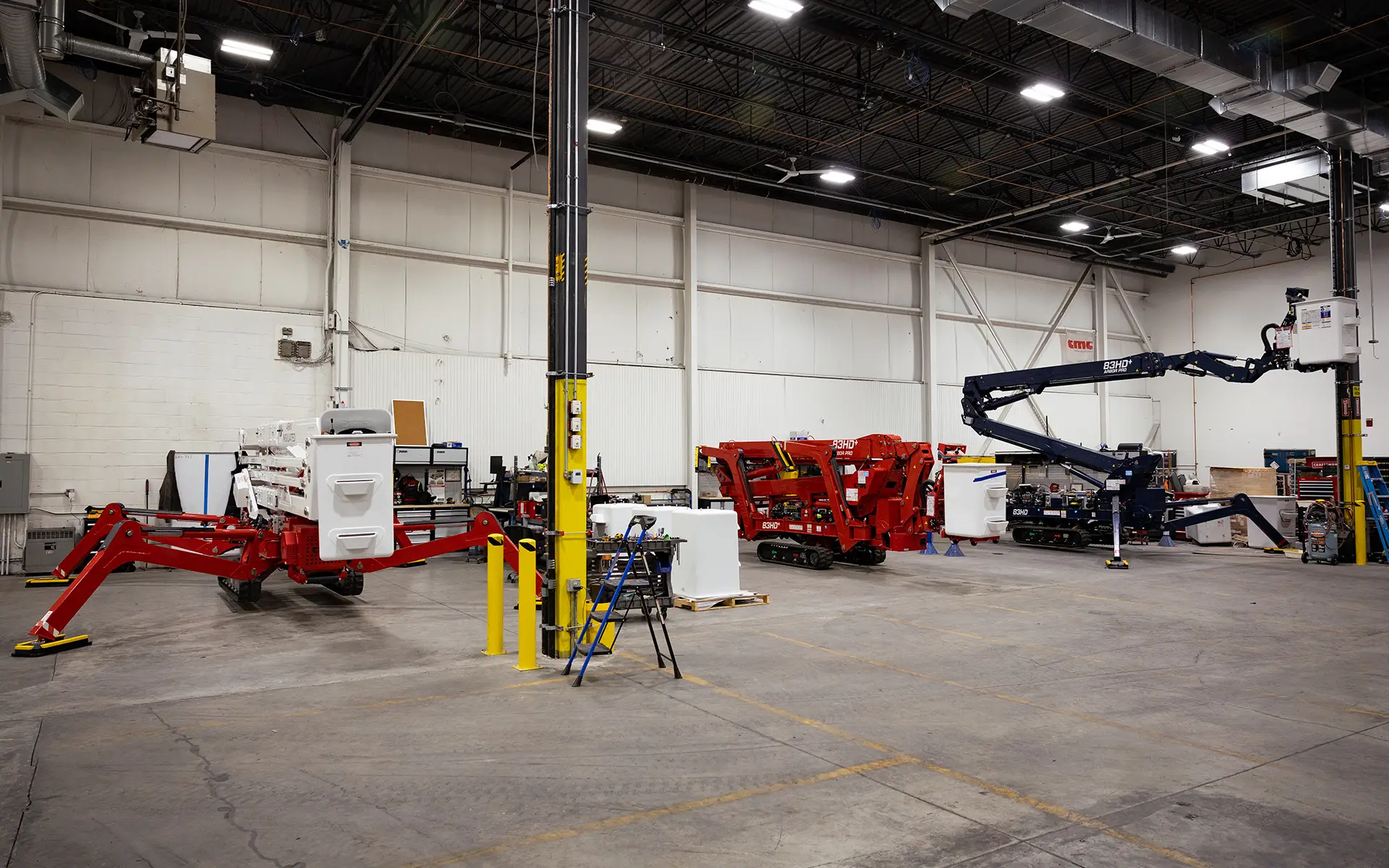 Industrial warehouse with three aerial work platforms in red and blue parked inside.