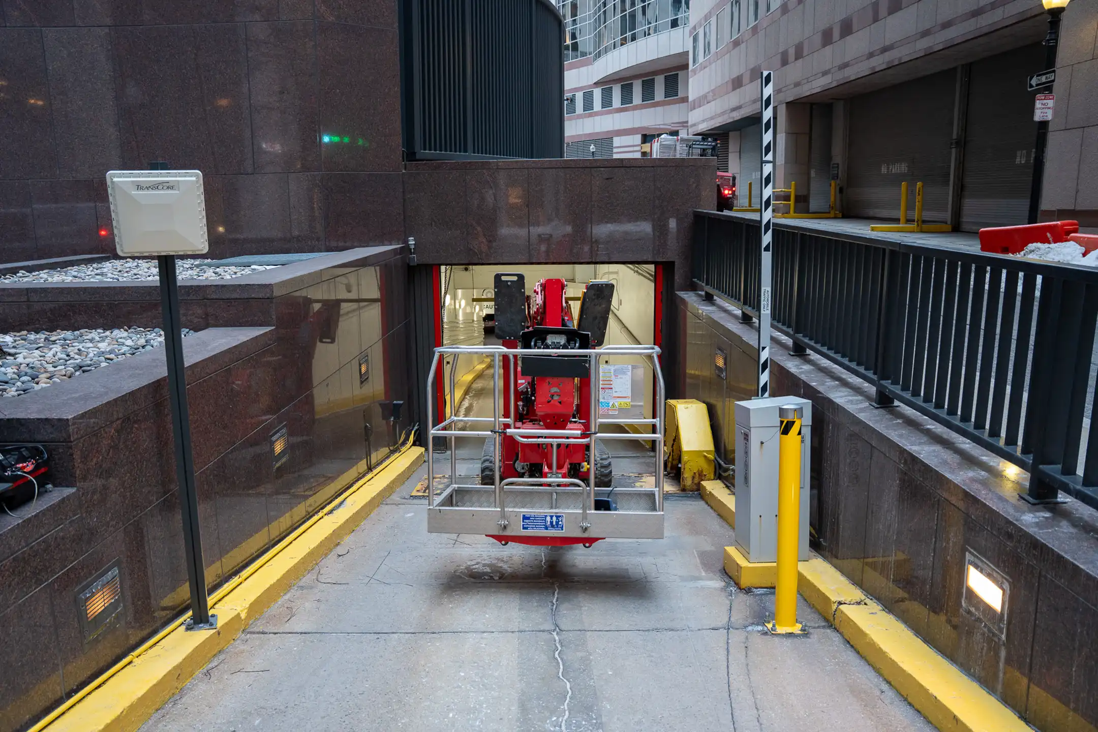Red scissor lift parked at the entrance of an underground parking garage.