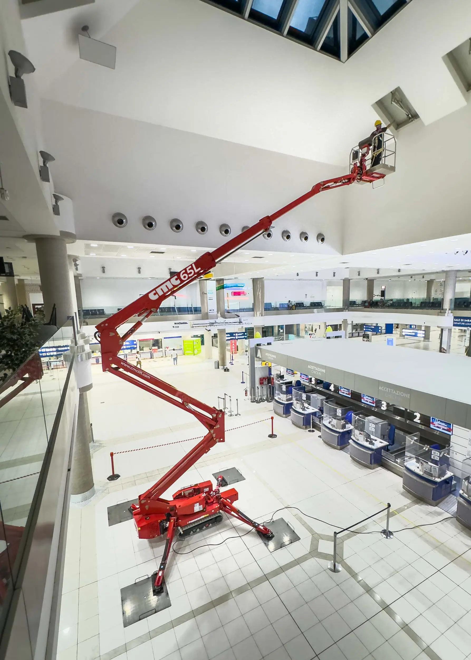 CMC 65L spider lift extended high inside airport terminal, worker in basket.
