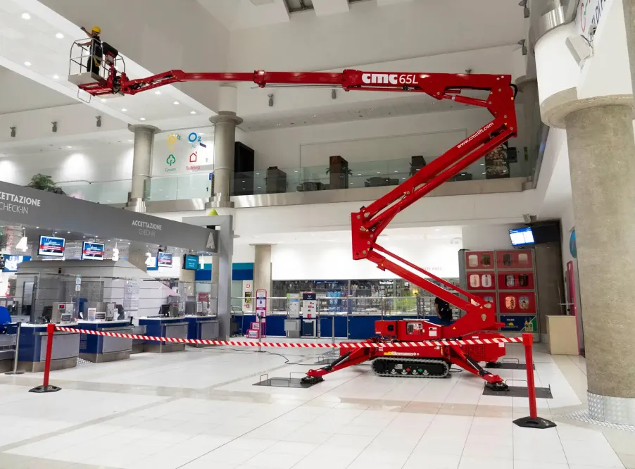 Two workers on a red CMC 65L mobile lift inside a large, modern building lobby.