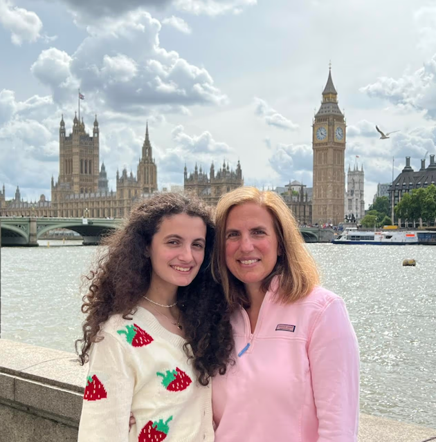 Two women smiling by the River Thames with Big Ben and the Houses of Parliament in London behind them.