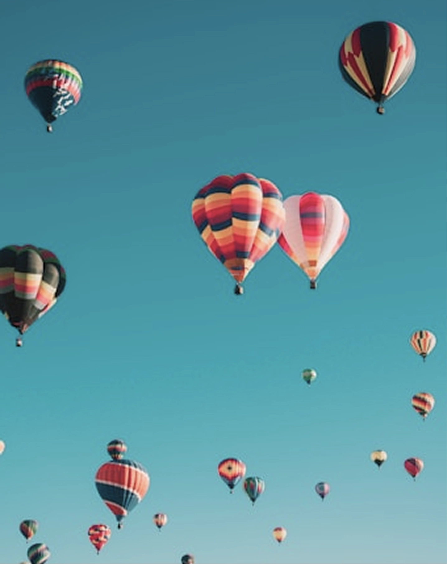 Multiple colorful hot air balloons floating in a clear blue sky.