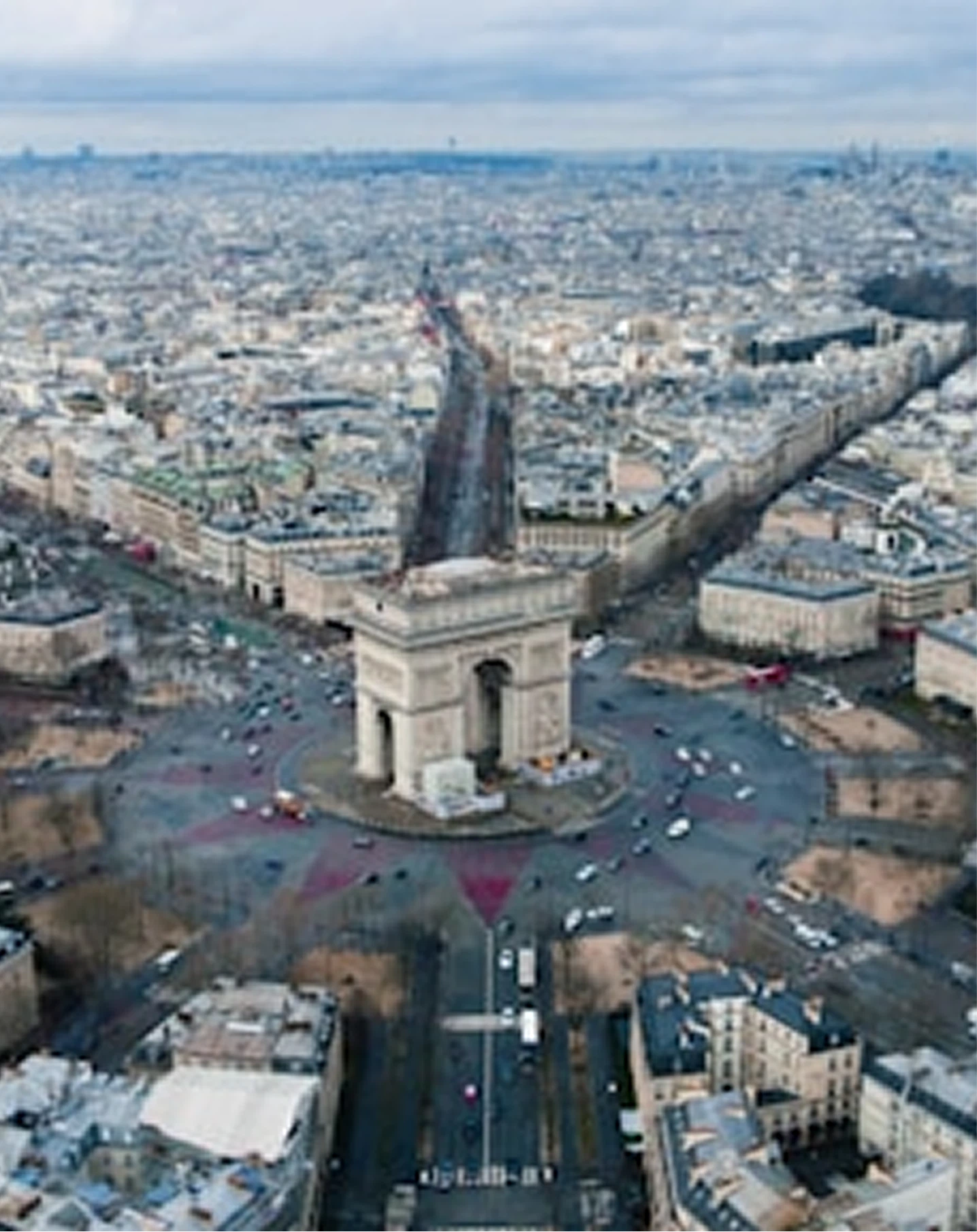 Aerial view of the Arc de Triomphe surrounded by traffic roundabout in Paris with cityscape background.