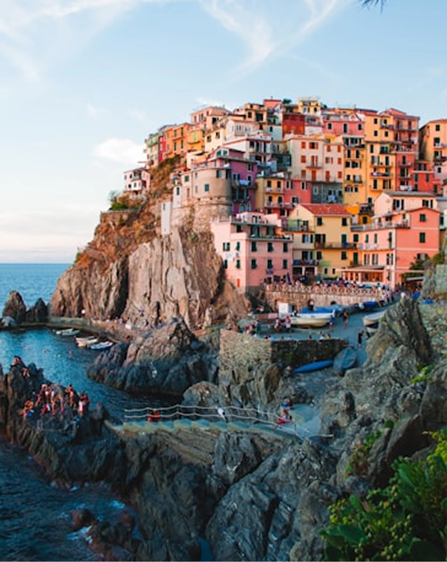 Colorful houses stacked on rocky cliffs by the sea with people near boats and water.