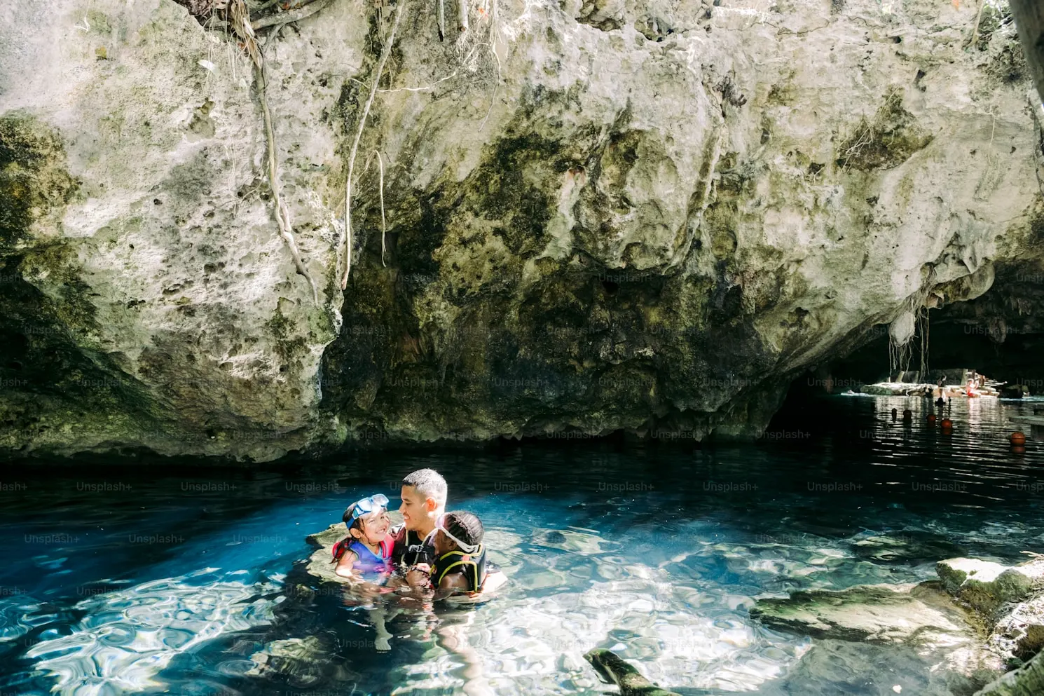 Three people wearing snorkeling gear in clear water inside a rocky cave.