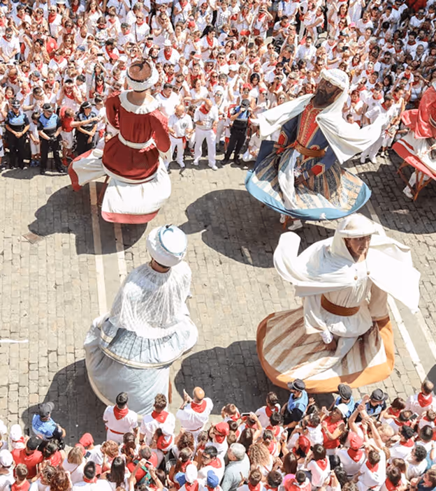Four people dressed in traditional large colorful costumes dancing in a crowded outdoor plaza.