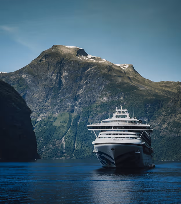 Cruise ship sailing in calm waters surrounded by towering green mountains under a clear sky.