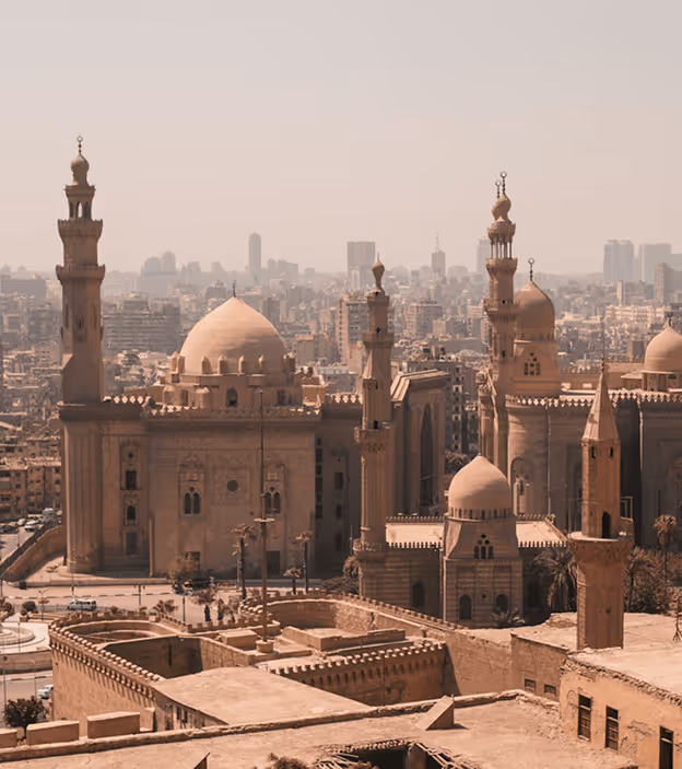 View of ancient Islamic architecture with domes and minarets in a cityscape under a hazy sky.