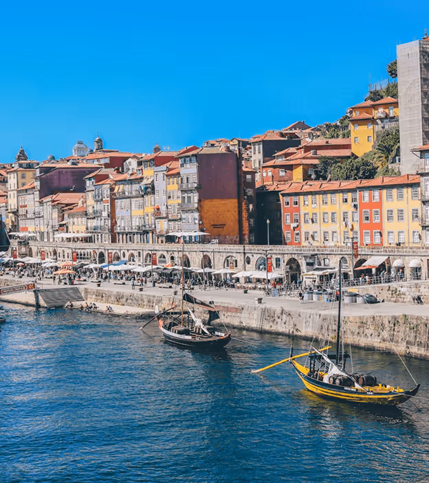Colorful waterfront buildings with outdoor cafes and boats on calm blue water on a sunny day.