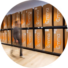 A person walking past shelves filled with large orange boxes labeled 'Emma'.