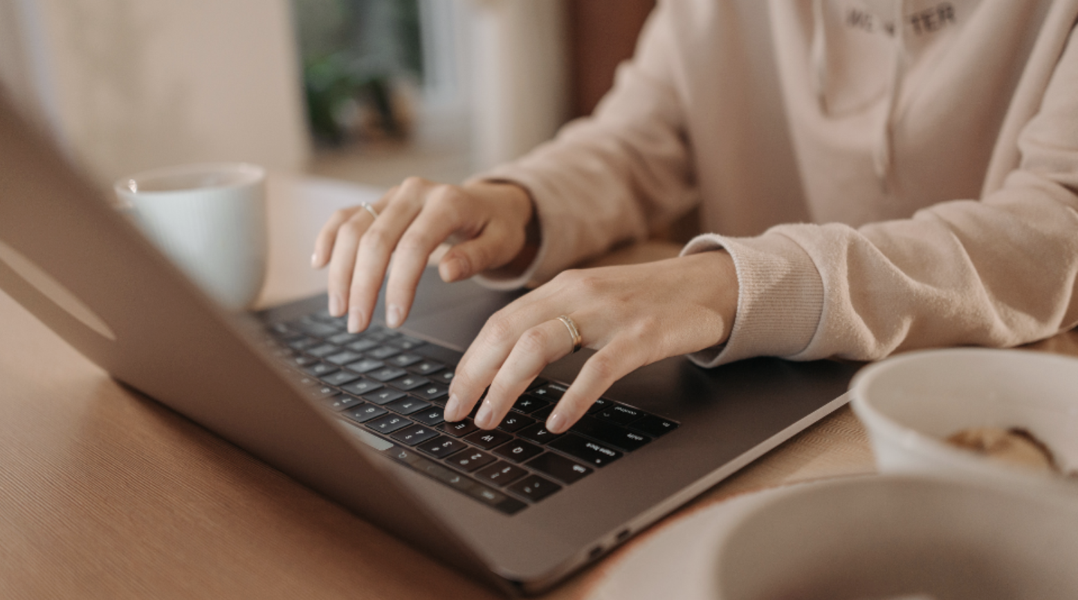 a person typing on a laptop computer with a cup of coffee in front of them