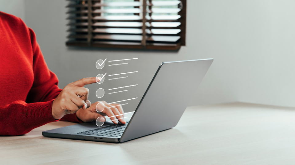 A person typing on a laptop on a table with a checklist coming off the screen