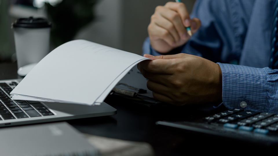 A person holding a piece of paper while sitting at a desk with a laptop