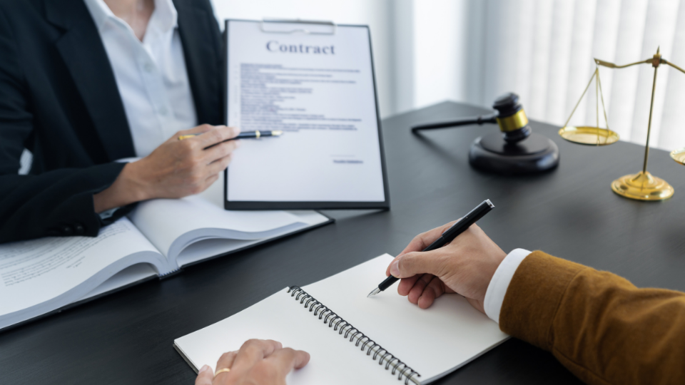 Two people sitting across from each other at a table with a contract and notepad placed between them