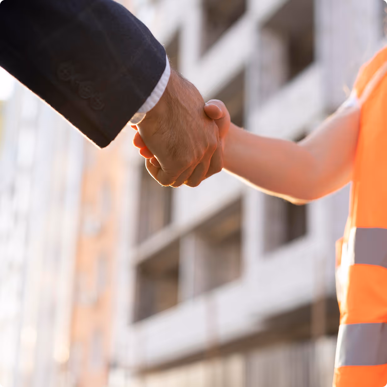 Handshake between a person in a business suit and a worker in an orange safety vest near a construction site.