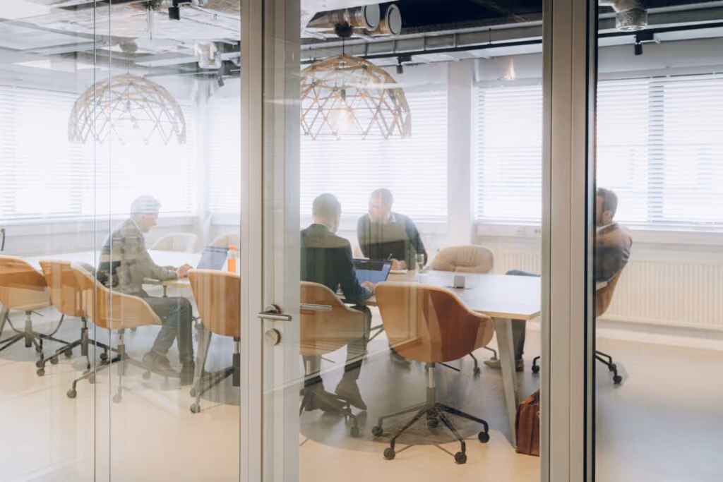 Four business people having a meeting around a table in a glass-walled office room.