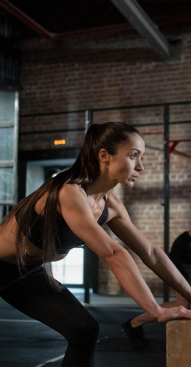 Two people in athletic wear perform push-up exercises on large wooden boxes in an industrial-style gym. The atmosphere is focused and intense.