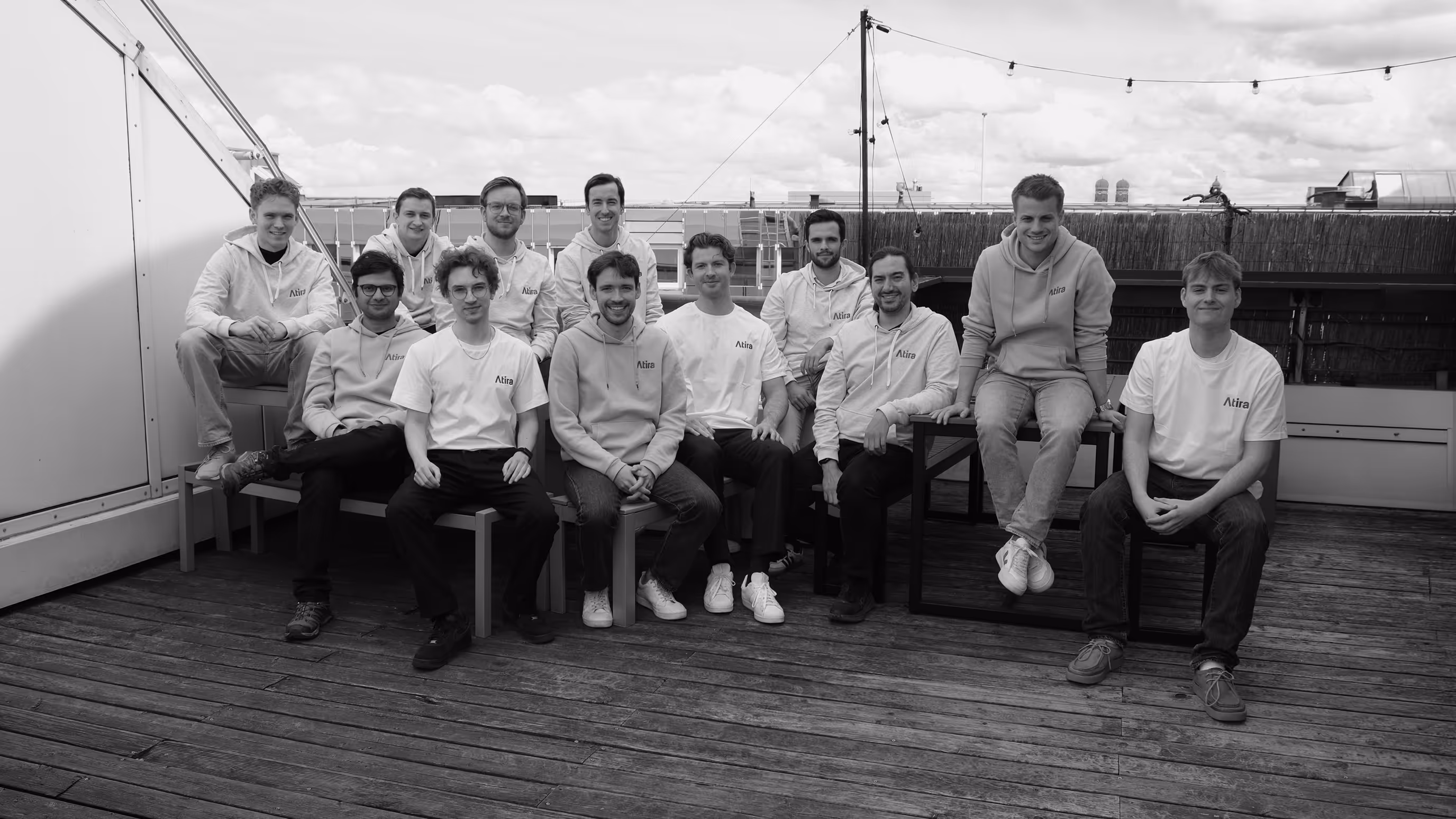 Group of Atira team members wearing Atira hoodies and t-shirts sitting on chairs on a rooftop deck.