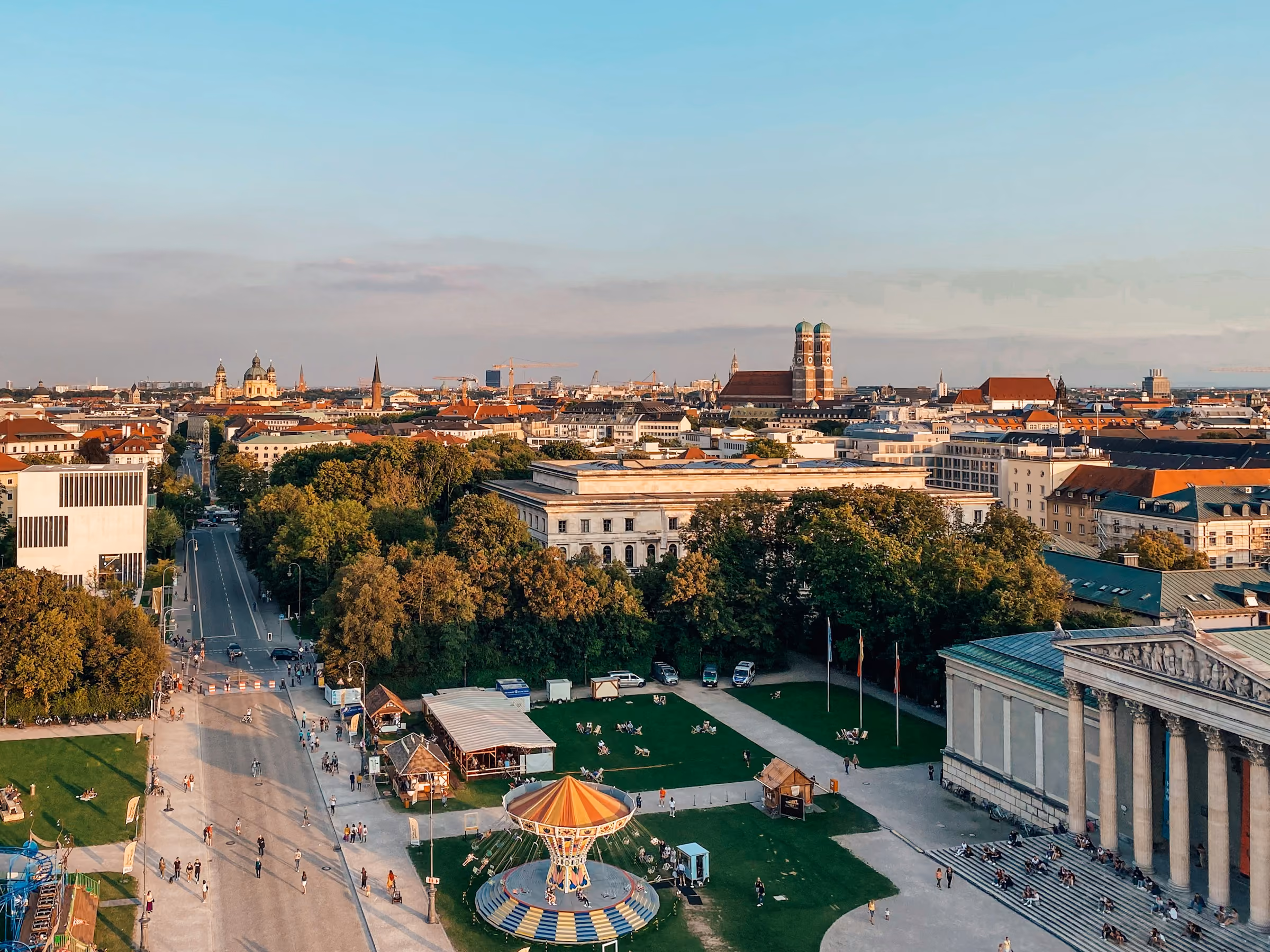 Munich skyline with historic buildings, a carousel, green parks, and people strolling in the late afternoon.