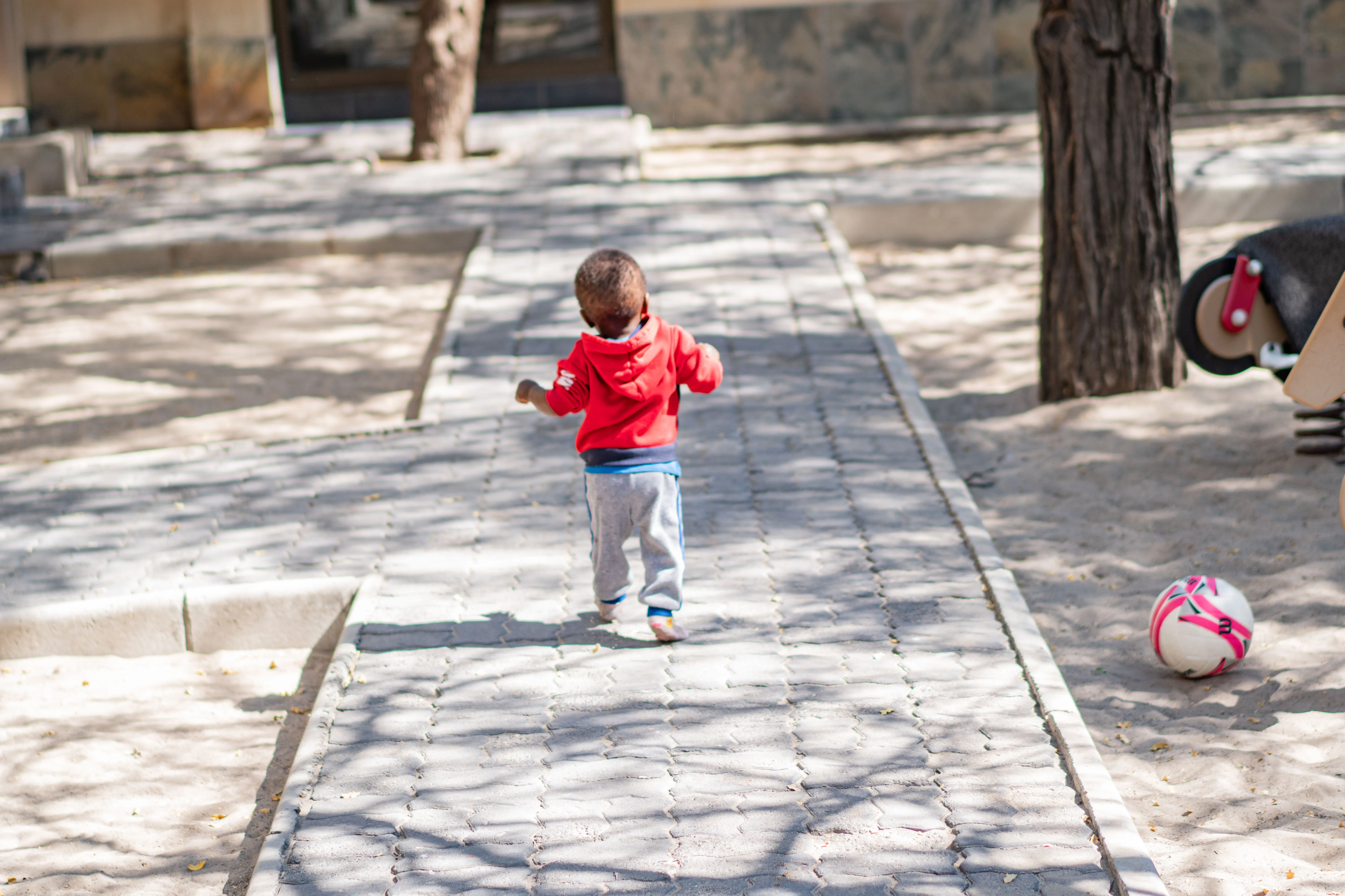 A toddler walking along a paved path at Lorato House, seen from behind