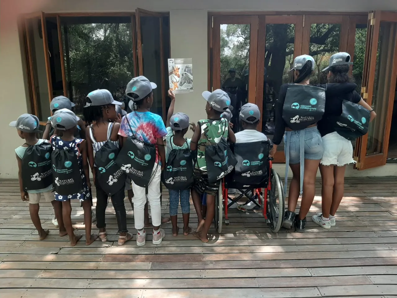 Children from Lorato House on an outing with donated caps and backpacks, seen from behind