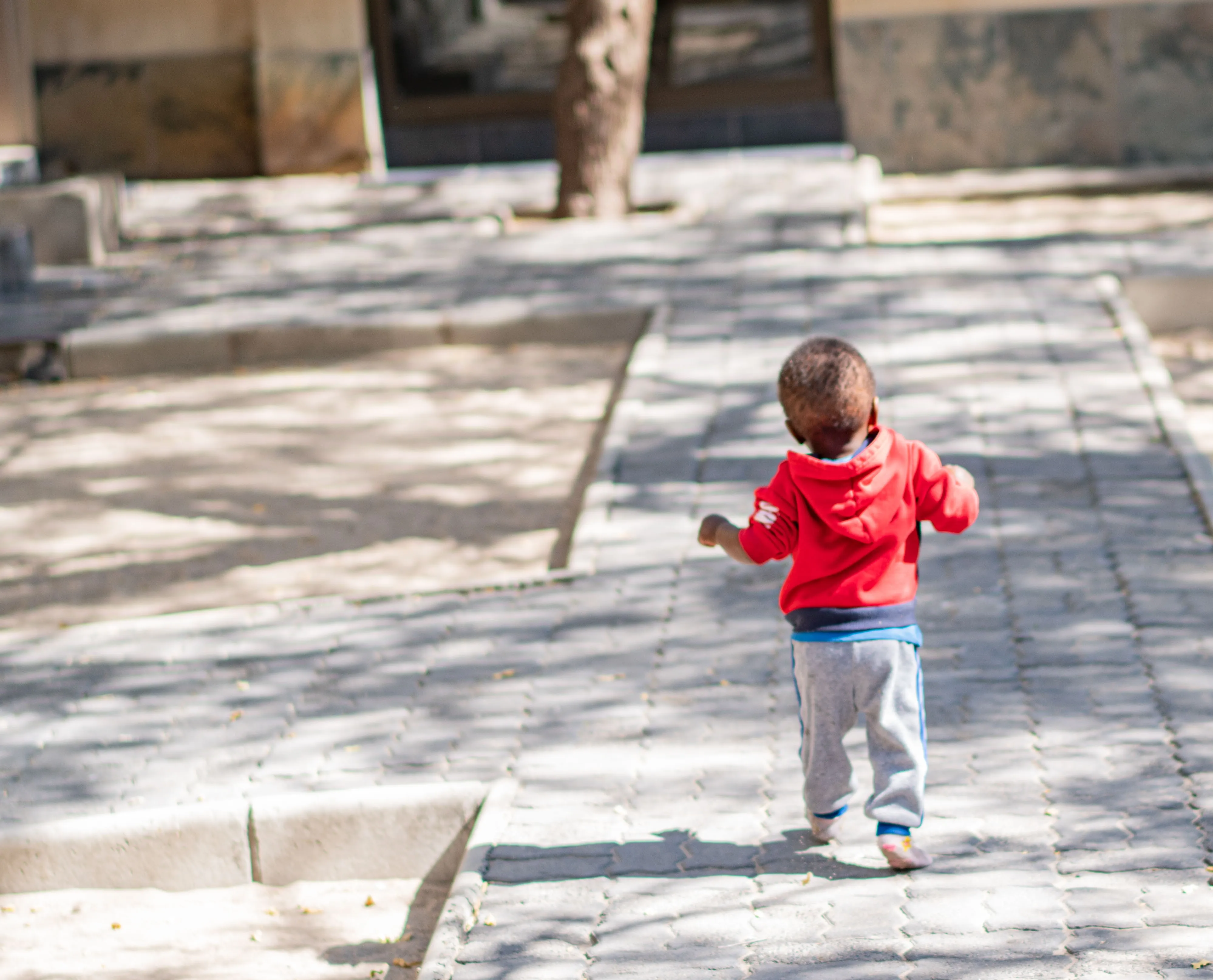 A toddler walking along the paved path at Lorato House, seen from behind