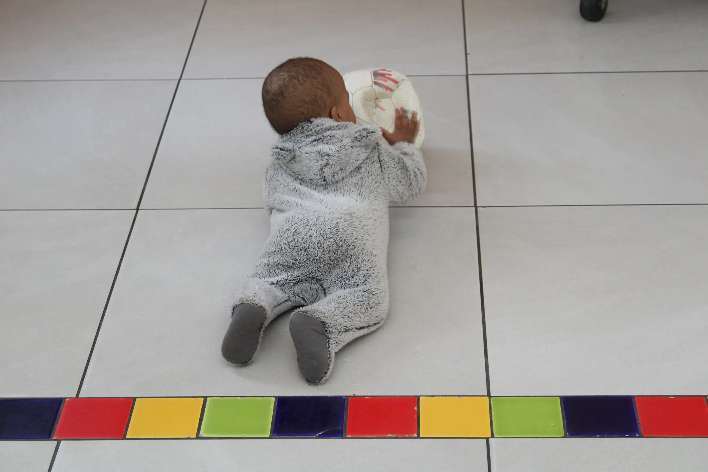 A baby lying on the floor playing with a ball at Lorato House