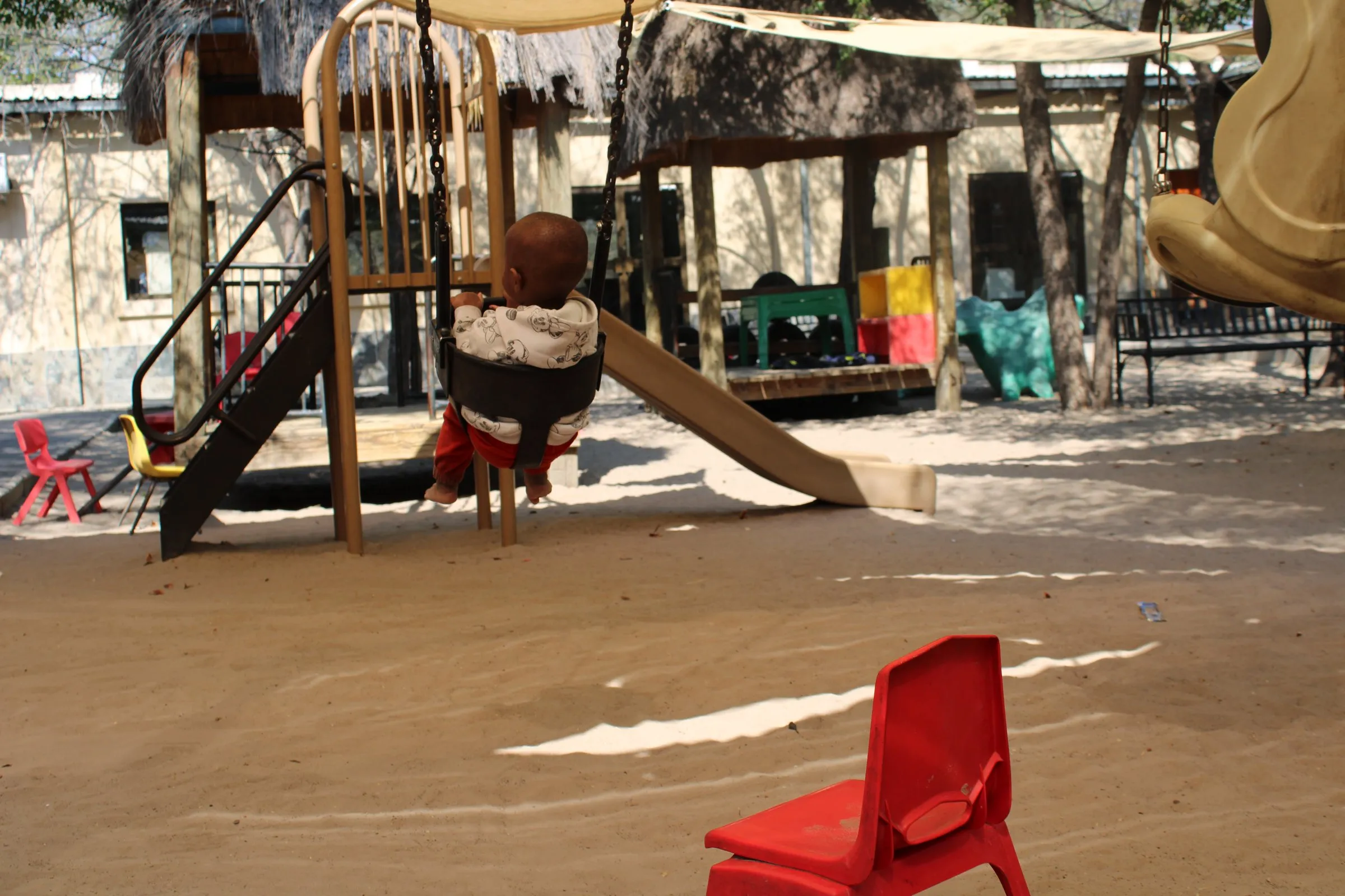 A young child on a swing in the Lorato House playground, seen from behind